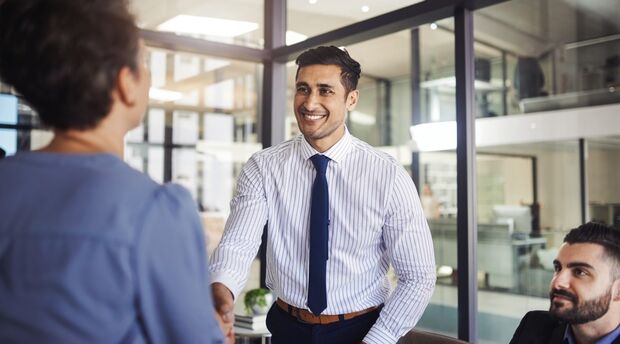 Two colleagues seated at a table engaging in conversation with a colleague standing nearby