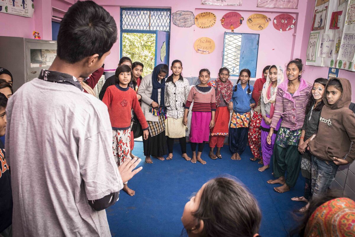 Man talking to a group of children in a room with pink walls 