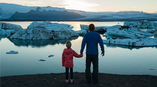 Parent and child holding hands looking at icebergs in the horizon