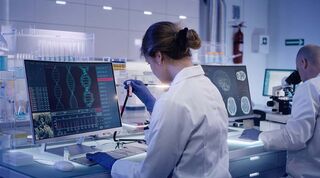 Scientist in a lab looking at a test tube in front of a computer screen