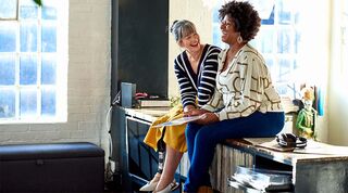 Two women sitting on top of a sideboard laughing