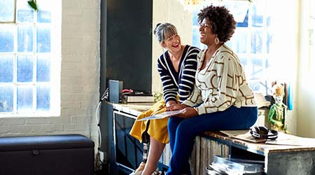 Two women sitting on top of a sideboard laughing