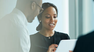 Two smiling colleagues standing together looking at an iPad