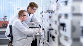 Side angle view of two scientists in a lab at a desk, analysing what’s in front of them