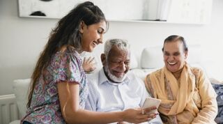 Young person smiling showing smiling older couple their mobile phone