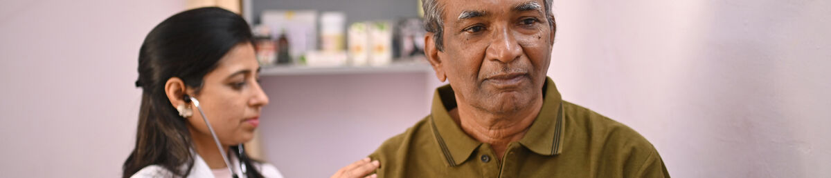 Health practitioner holding a stethoscope against an older patient’s back