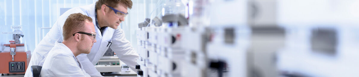 Side angle view of two scientists in a lab at a desk, analysing what’s in front of them