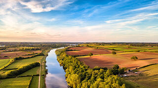 View from above of vibrant field landscape divided by a long river with a blue sky and light clouds