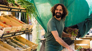 Smiling, bearded man arranges vegetables at an open market stall