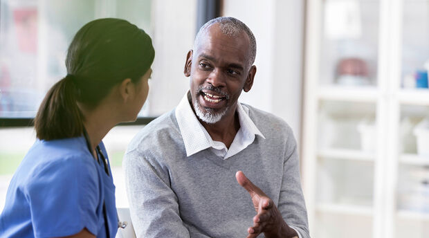 Two colleagues seated at a table engaging in conversation with a colleague standing nearby