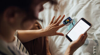 Person reading data on mobile phone while using oximeter to check blood condition.